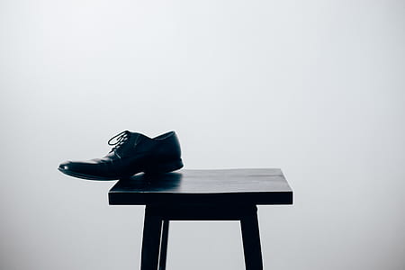 unpaired black dress shoes on black stool thumbnail