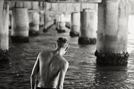 grayscale photography of man walking on water under bridge thumbnail