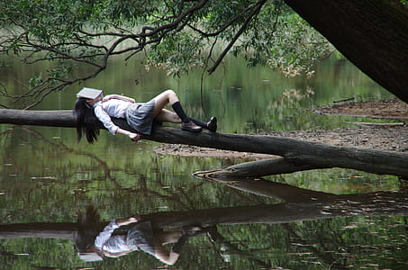 woman in white long-sleeved shirt lying on branch of tree during daytime thumbnail