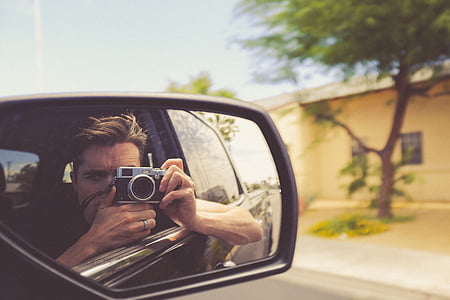 time lapse photography of person riding car while taking picture of vehicle side mirror with self reflection during daytime thumbnail