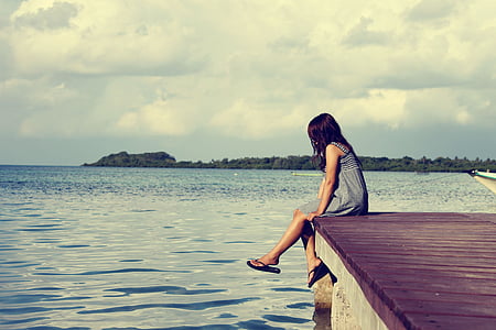 woman in gray dress sitting on dock during cloudy daytime thumbnail