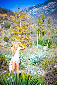 woman wearing white short-sleeved dress standing in the forest facing towards gray mountains at daytime thumbnail