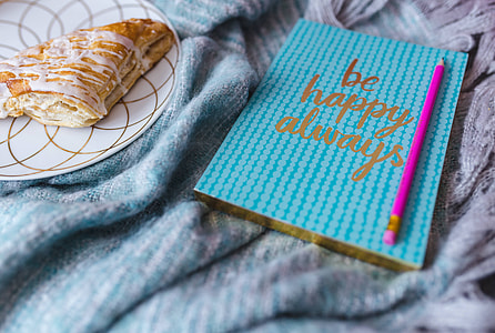 Blue notebook with a pink iPhone, headphones and a sweet bun thumbnail
