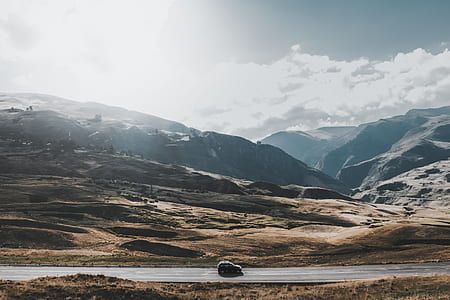 vehicle crossing asphalt road between grass field near mountain during daytime thumbnail