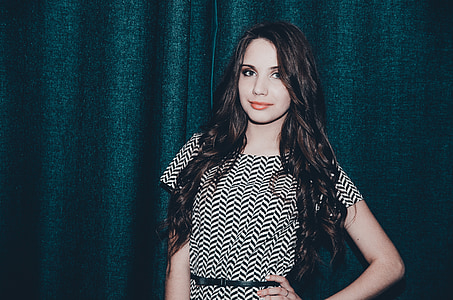 woman wearing white and black crew-neck short-sleeved dress standing in front of black curtain thumbnail