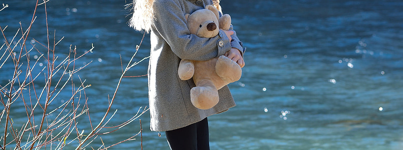 woman holding brown teddy bear near river thumbnail