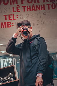 Man Holding Camera Beside Text Printed Wall thumbnail