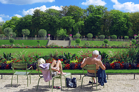 man and woman sitting on armchair in front of open field with flowers and trees under white and blue cloudy skies thumbnail