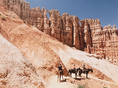 three men riding horse near outcrop thumbnail