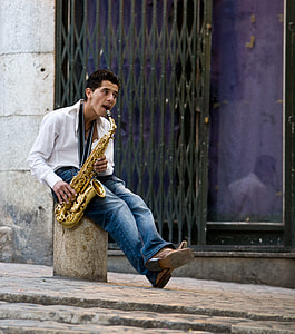 man sitting on post playing saxophone near building during daytime thumbnail