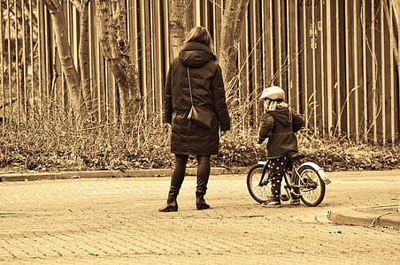 woman standing beside child riding bike thumbnail