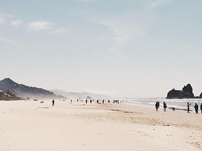seashore with people walking near mountain under blue sky thumbnail