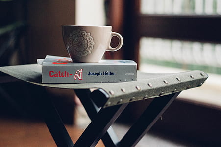 white ceramic cup on book placed on folding chair thumbnail