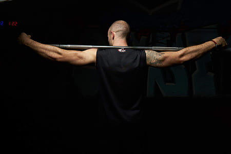 man wearing black sleeveless top holding gray barbell rod thumbnail