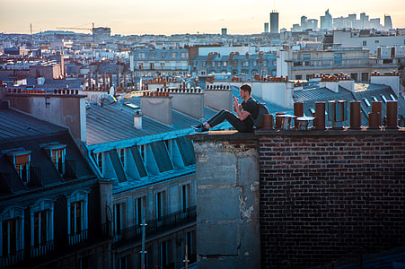 aerial photo of man sitting on rooftop ledge during daytime thumbnail