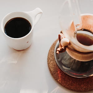 white ceramic cup with coffee near clear glass pitcher on table thumbnail