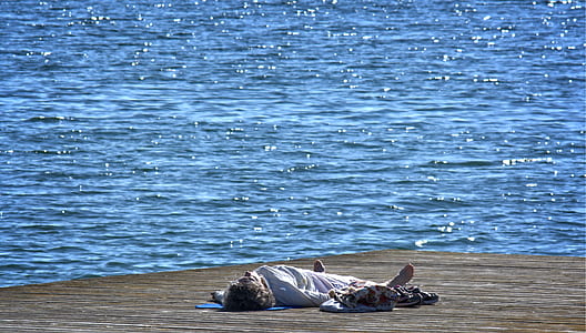 man in white long-sleeved shirt lying on brown sand near body of water during daytime thumbnail