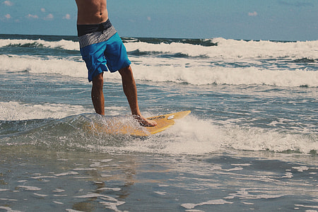man with blue board shorts riding yellow skimboard on the beach thumbnail