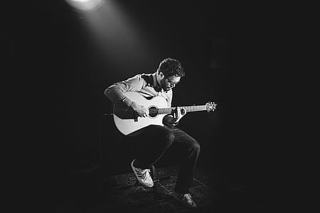 grayscale photography og man sitting on chair while playing acoustic guitar thumbnail