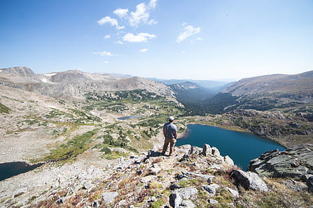 man standing on cliff facing lake thumbnail