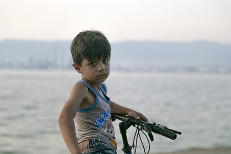 selective focus photography of boy riding bike near body of water thumbnail