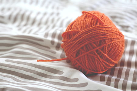 red yarn ball on top of blue and white striped textile thumbnail