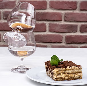 two clear wine glasses beside chocolate cake plate on table with white tablecloth thumbnail