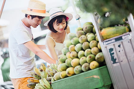 man and woman wearing hat standing in front of fruits during daytime thumbnail