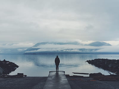 silhouette of person standing in front of body of water thumbnail