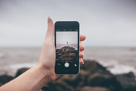 person holding black iPhone 4 while taking photo of sea shore during daytime thumbnail