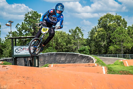 man wearing racing jacket, pants, and helmet performing bicycle stunts on brown soil during daytime thumbnail