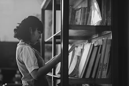 Grayscale Photo of a Woman Holding a Book Inside the Library thumbnail