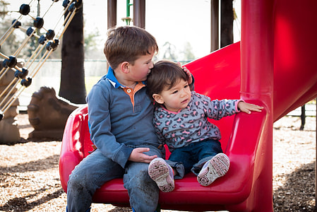 girl and boy sitting on red plastic slide thumbnail