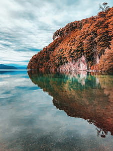 calm waters near rock cliffs and brown leaved trees thumbnail
