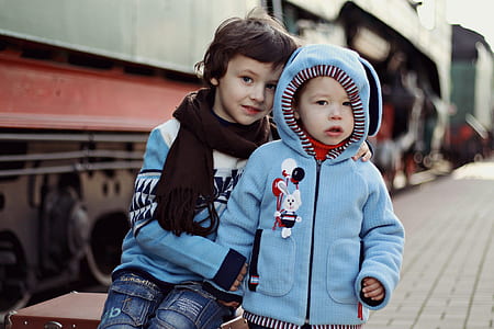 boy sitting beside another boy in blue zip-up hoodie standing outdoors thumbnail