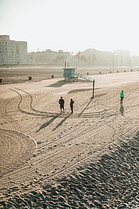 three people standing on gray sand near buildings thumbnail