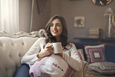 A young woman sitting on the couch holding a coffee mug in her hand in the living room thumbnail