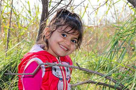 girl in red and white jacket smiling near brown wooden trees thumbnail