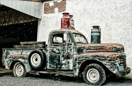black and brown rusted classic pickup truck park near gray wall with thee assorted-color milk churns on top photo taken during daytime thumbnail