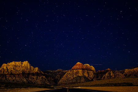 empty highway overlooking brown rock mountain under stars at nighttime thumbnail