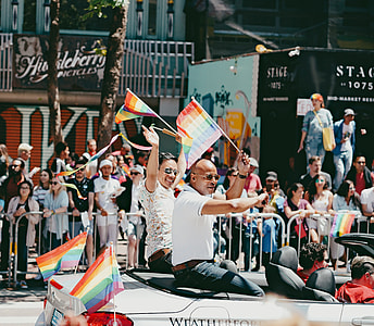two men riding a convertible coupe holding LGBT flaglets during daytime thumbnail