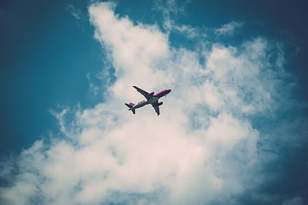 low angle photography of plane flying with cloudy sky thumbnail
