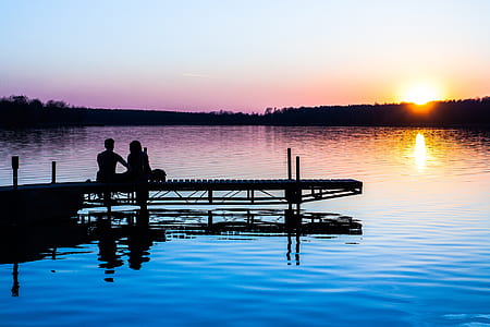 silhouette of man and woman sitting on dock thumbnail