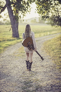 walking woman holding brown guitar at daytime thumbnail