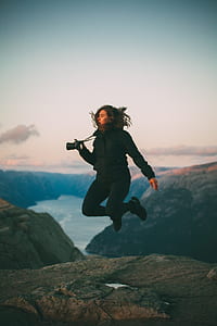 woman jumping above mountain while carrying black DSLR camera thumbnail