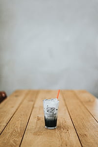 ice and beverage filled drinking glass with straw on wooden table thumbnail