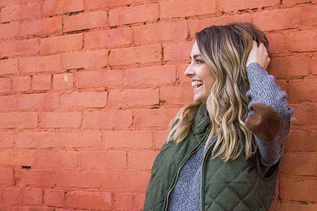 woman holding her hair while leaning on red brick wall thumbnail