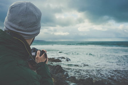 man taking photo of ocean wave during gray clouds thumbnail