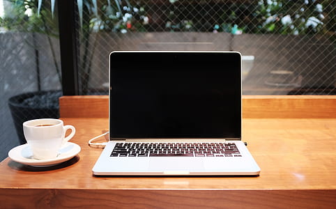 silver laptop computer beside ceramic teacup on wooden table thumbnail