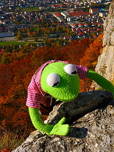 green frog plush toy climbing on brown stone cliff thumbnail